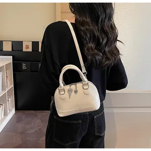 Détail d'un sac à main beige en forme de coquille avec breloques cœur et clé en métal