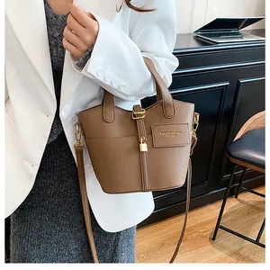 Détail d'un sac seau en cuir grainé marron foncé avec boucle dorée sur un mannequin chic