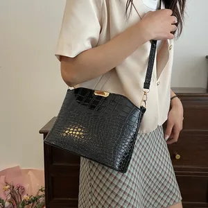 Glossy black crocodile pattern shoulder bag with gold clasp shown on a model