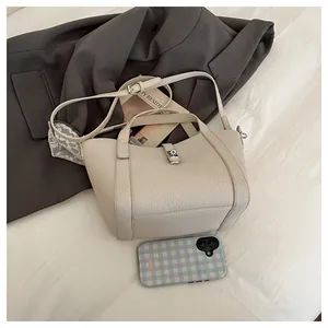 Vue à plat d'un sac à main crème en cuir grainé avec boucle argentée sur un lit