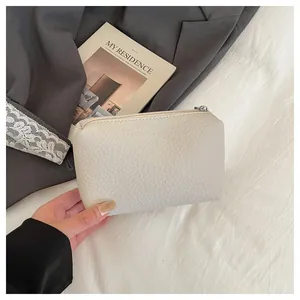 Gros plan sur la mini pochette crème avec texture litchi et fermeture éclair argentée