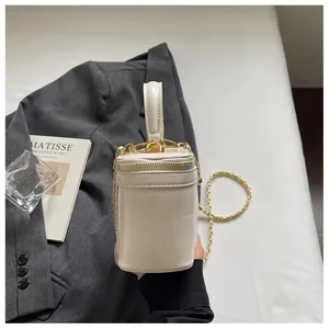 Detailed side view of white cylinder handbag with gold chain strap and dual zippers