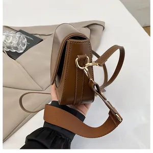 Detail of brown saddle bag with gold hardware and stylish wide woven shoulder strap