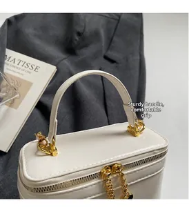 Close-up of sturdy top handle and heart charm zipper on creamy white vanity bag