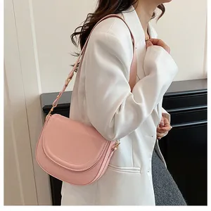 Side view of pink saddle crossbody bag styled with a white blazer for a commute look