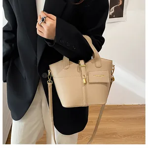 Détail du sac seau beige en cuir grainé avec finitions dorées porté avec un blazer noir