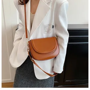 Detailed view of a brown leather saddle bag styled with a white blazer for a classic look