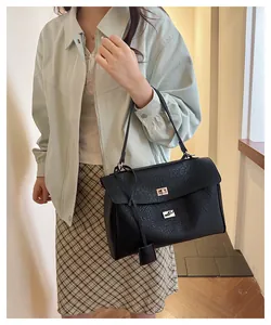 Détail d'un sac à main en cuir noir avec un fermoir doré et une bandoulière réglable