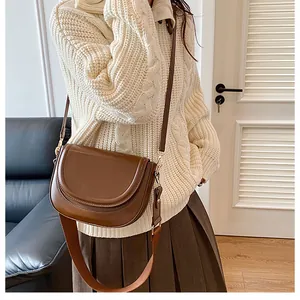 Detail of dark brown saddle bag with dual straps worn over a white sweater