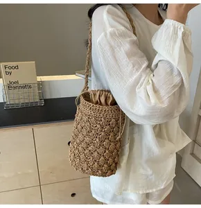Detail of straw bucket bag featuring fine weaving and beige drawstring lining worn by a model