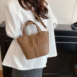 Sac seau marron grainé avec boucle dorée et bandoulière réglable porté par un mannequin