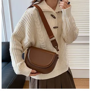 Close-up of brown leather saddle bag with wide strap and gold hardware on model