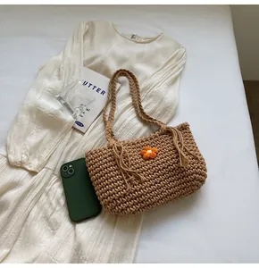 Close-up of woven straw tote bag featuring a 3D orange knit flower and braided handles