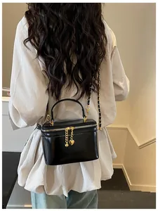 Detail of glossy black patent leather mini bag with gold chain strap and heart charm