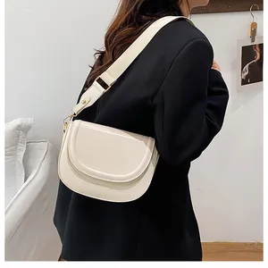 Detail of a creamy white saddle bag with golden hardware and wide strap worn by a model