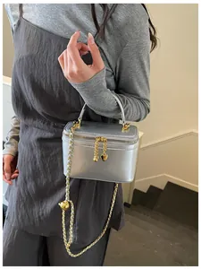 Detail of silver matte box bag featuring golden heart pendant and leather chain strap