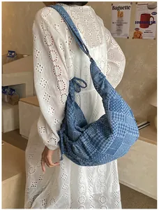 Detail view of denim crescent bag featuring patchwork plaid patterns and a wide shoulder strap