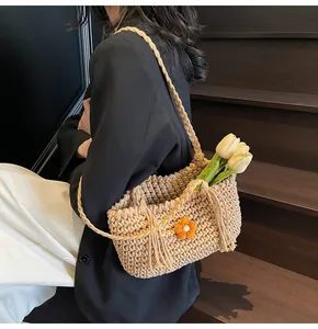 Detail of hand-woven beige crochet tote bag featuring an orange flower and tassel