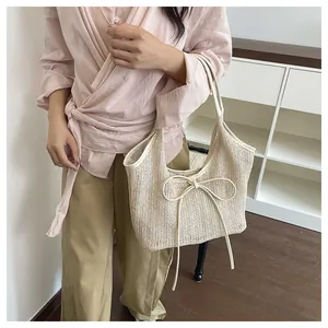 Détail d'un sac d'épaule en paille tressée avec un grand nœud décoratif sur le côté