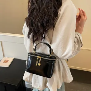 Glossy black box-shaped crossbody bag with gold heart charm and chain strap detail