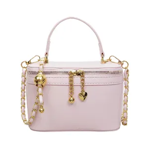 Pale pink box shape handbag with gold chain strap and heart charm on white background