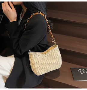 Dettaglio borsa a tracolla in paglia intrecciata beige con bordo a onde e catena