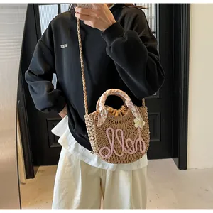 Close-up of straw woven handbag with pink hello text, daisy detail and floral scarf