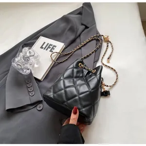 Detail of quilted leather bucket bag with gold chain strap and metallic decorative ball