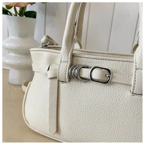 Gros plan détaillé du cuir grainé beige et de la boucle métallique sur le sac à main