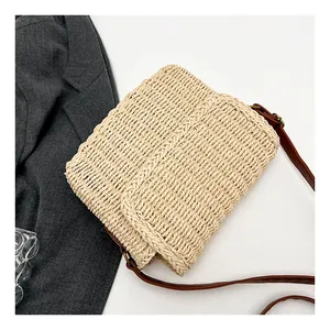 Detail of hand-woven beige straw bag with brown leather strap and bronze metal rings