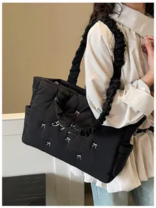 Detail of black quilted tote bag featuring white bow embroidery and ruffled shoulder strap