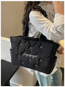 Detail of black quilted nylon tote bag featuring white embroidered bows and soft texture