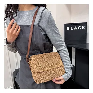 Detail view of a handmade straw crossbody bag with brown leather strap on a model