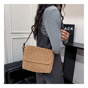 Detail of woven straw shoulder bag with brown leather strap worn by a model indoors