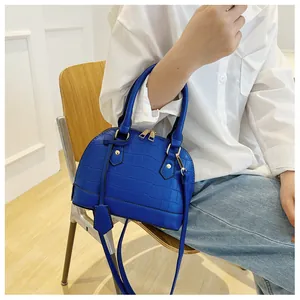 Blue crocodile pattern shell bag held by model wearing white shirt and blue jeans