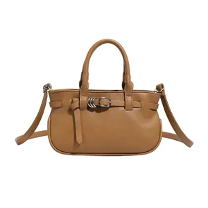 Sac à main marron en cuir grainé avec boucle en métal et bandoulière sur fond blanc uni
