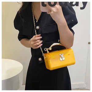 Detail of yellow acrylic box clutch with gold metal handle and chain strap on model