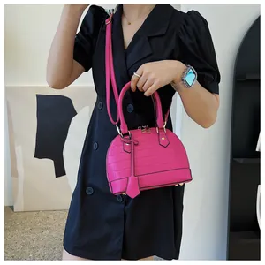 Hot pink crocodile pattern shell bag worn by a model in a black dress as a crossbody bag