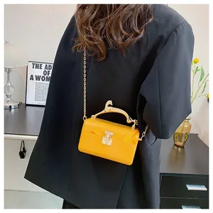Detail of bright orange acrylic handbag with gold animal-shaped handle and metal chain