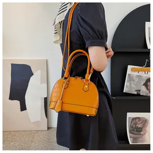 Detail of orange shell-shaped handbag featuring crocodile texture and gold hardware