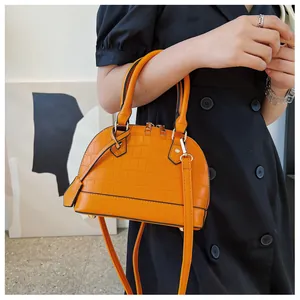 Close-up of bright orange shell bag featuring crocodile texture and gold hardware details
