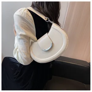 Détail du sac demi-lune crème avec boucles argentées porté à l'épaule par un mannequin