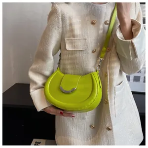Détail du sac bandoulière vert fluo en forme de croissant avec fermoir argenté sur manteau