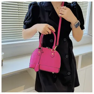 Magenta shell handbag with crocodile texture shown being carried by a model in a black dress