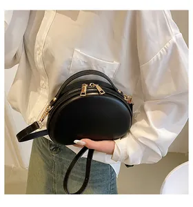 Détail d'un sac rond noir en cuir PU avec zips dorés porté par un mannequin en tenue décontractée