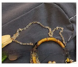 Détail de la poignée en bambou marron foncé et de la bandoulière en chaîne dorée brillante