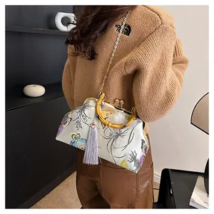 Détail du sac en satin brodé avec poignée en bambou, motifs floraux de papillon et gland