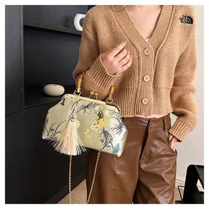 Détail du sac brodé en soie avec poignée en bambou, motif papillon et pompon blanc