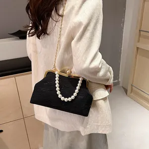 Sac coquille noir élégant avec poignée en perles et chaîne dorée porté par un mannequin