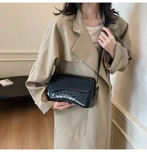 Nahaufnahme der schwarzen Lackhandtasche mit Krokoprägung und Goldverschluss am Model